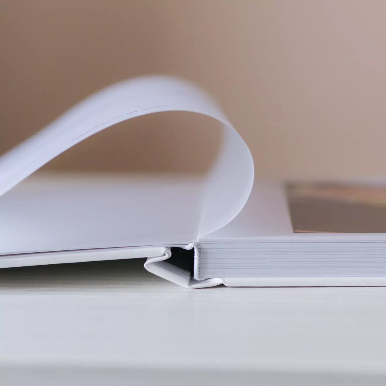 Close-up image of an open photobook with a thick, high-quality page being turned, showcasing the binding and paper quality. The background is softly blurred, emphasizing the photobook's craftsmanship.