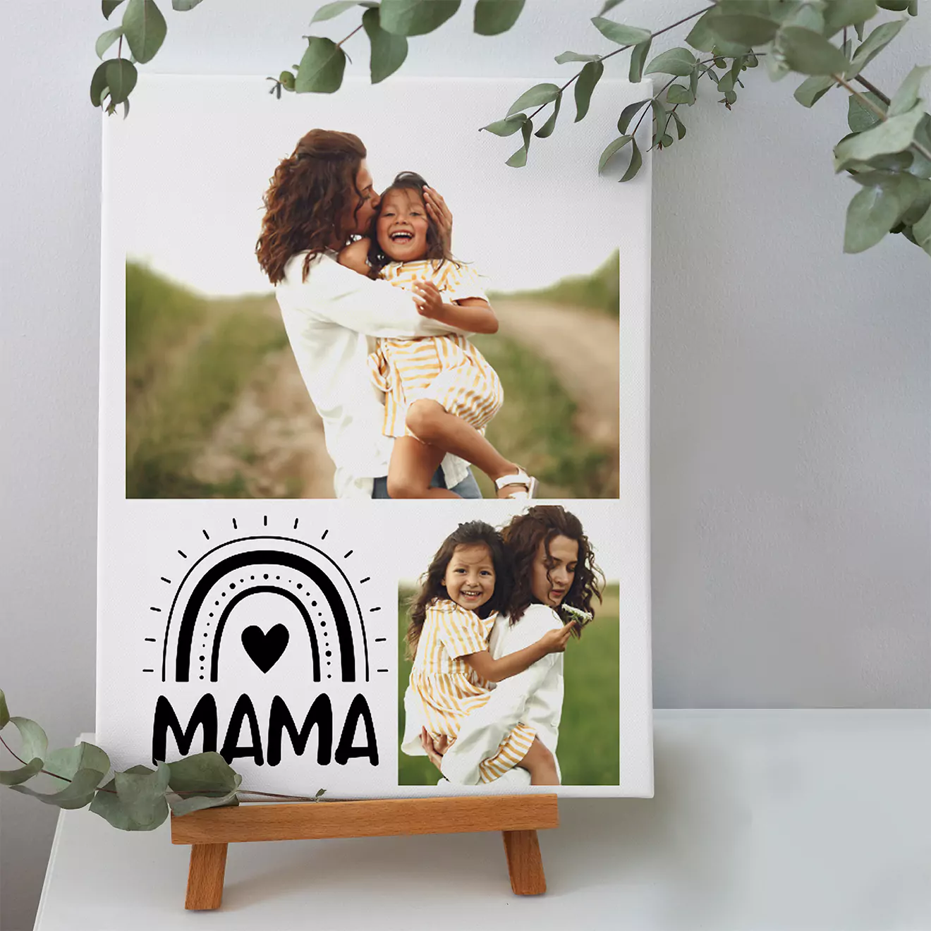 Personalised photo canvas featuring two images of a mother and child, with the word "MAMA" and a heart design. Displayed on a small wooden easel, surrounded by green foliage. Ideal for Mother's Day or family gifts.