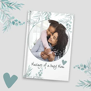 A personalised Mother's Day photobook titled 'Musings of a busy Mom' featuring a cover photo of a mother and child embracing, surrounded by a delicate floral design and heart accents.