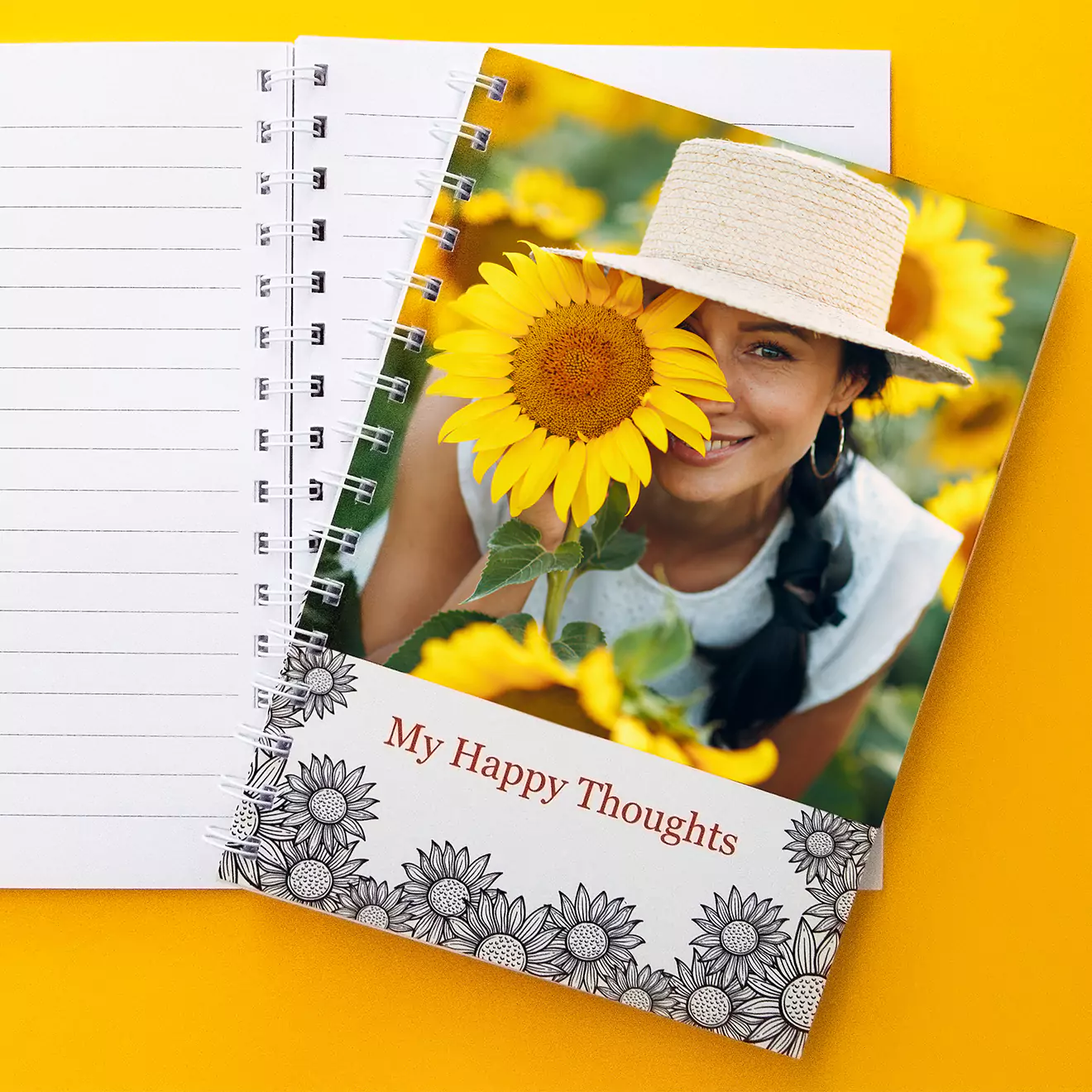 Personalised softcover notebook with a spiral binding, featuring a cover image of a smiling woman in a sunflower field and the text 'My Happy Thoughts.' The notebook is displayed on a yellow background.