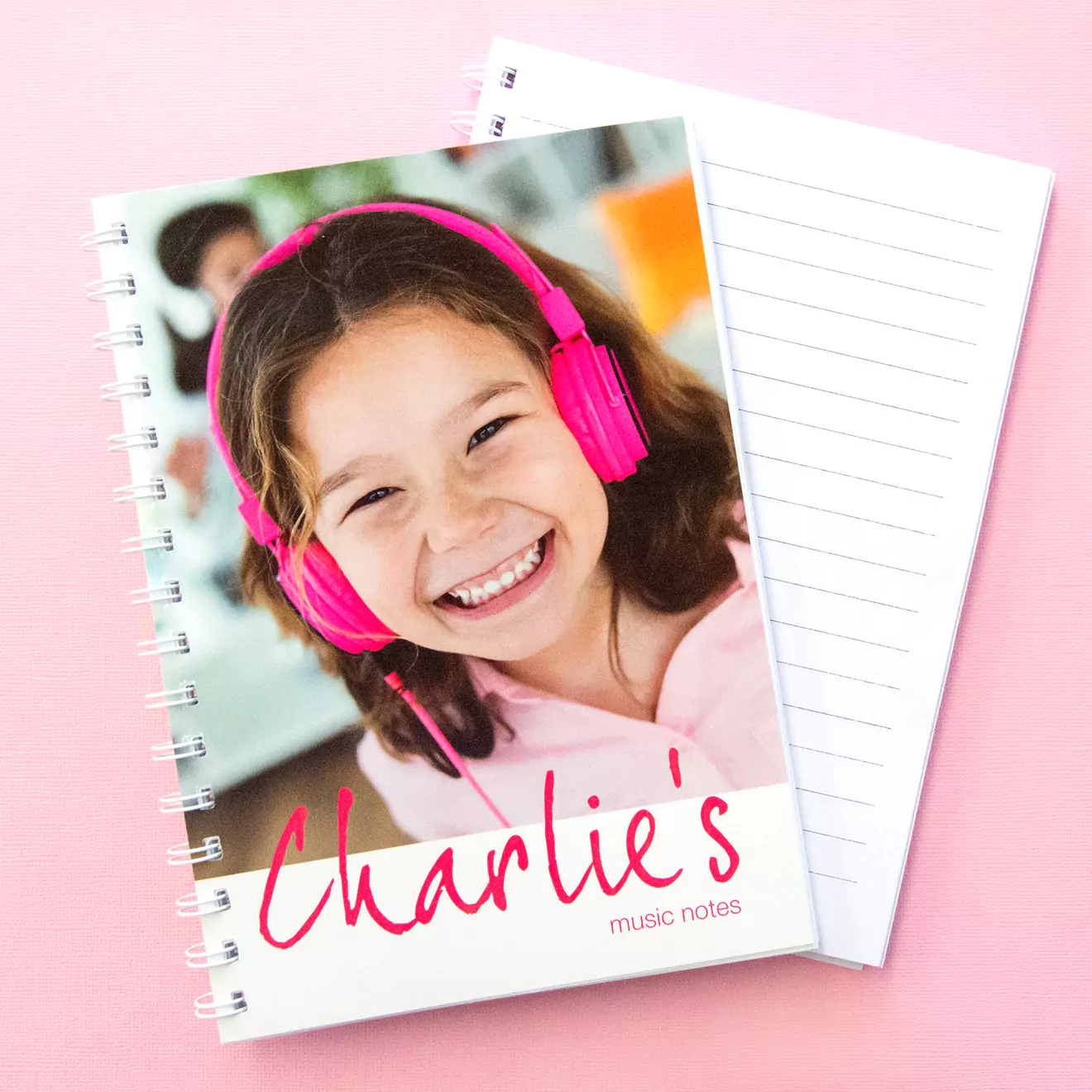 Personalised softcover notebook featuring a smiling child with pink headphones on the cover, labeled 'Charlie's music notes.' The notebook has a spiral binding and lined pages.