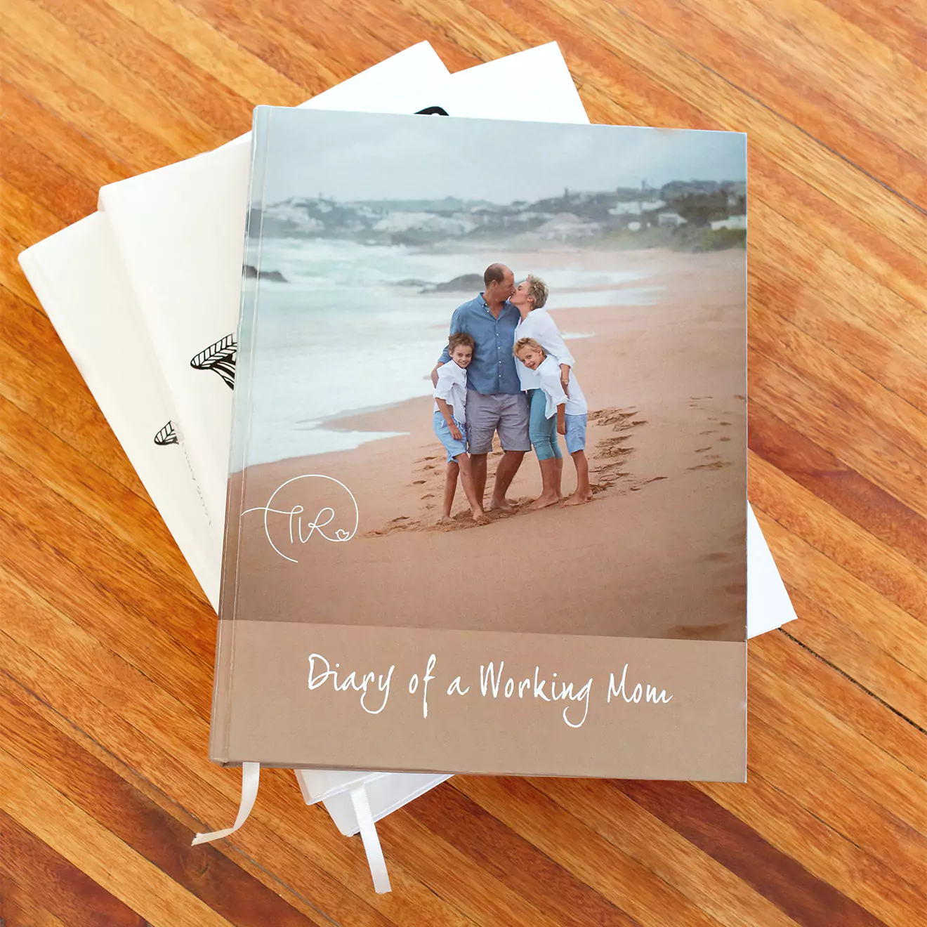 Personalised Diary, titled 'Diary of a Working Mom' featuring a cover image of a family on a beach, placed on a wooden surface with two other photo diaries partially visible underneath.