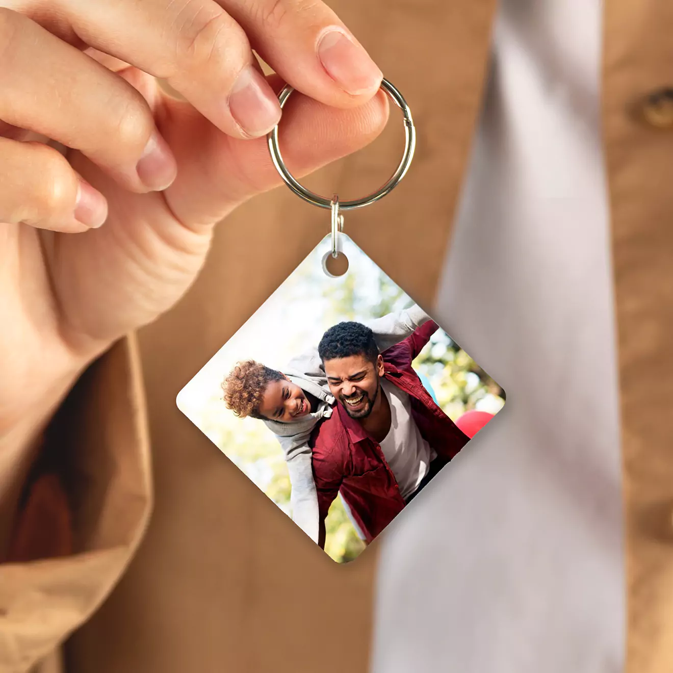 Close-up of a hand holding a personalised keyring featuring a square photo of two smiling individuals. The keyring has a metal ring and a glossy finish, making it a perfect gift idea for various occasions.