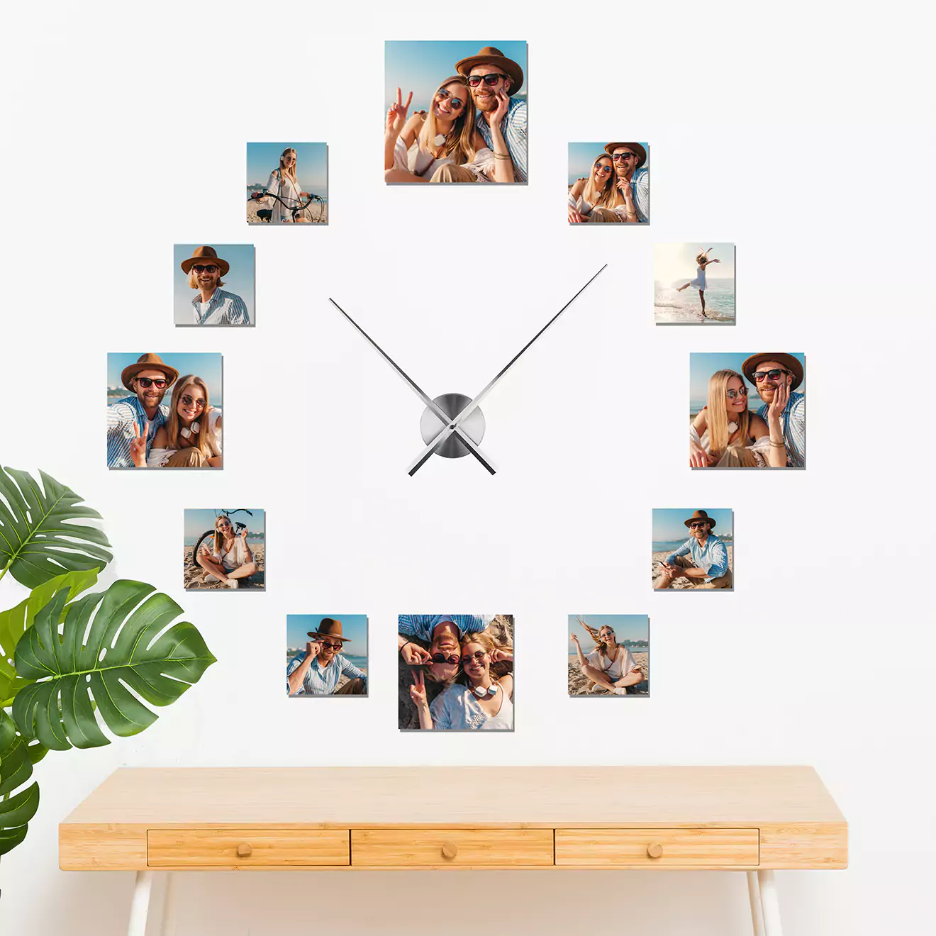 Wall art clock featuring twelve photo frames arranged in a circular pattern around a central clock mechanism. Each frame displays a different photo, creating a personalized and functional decor piece. The clock is mounted above a wooden console table with a green plant on the side.