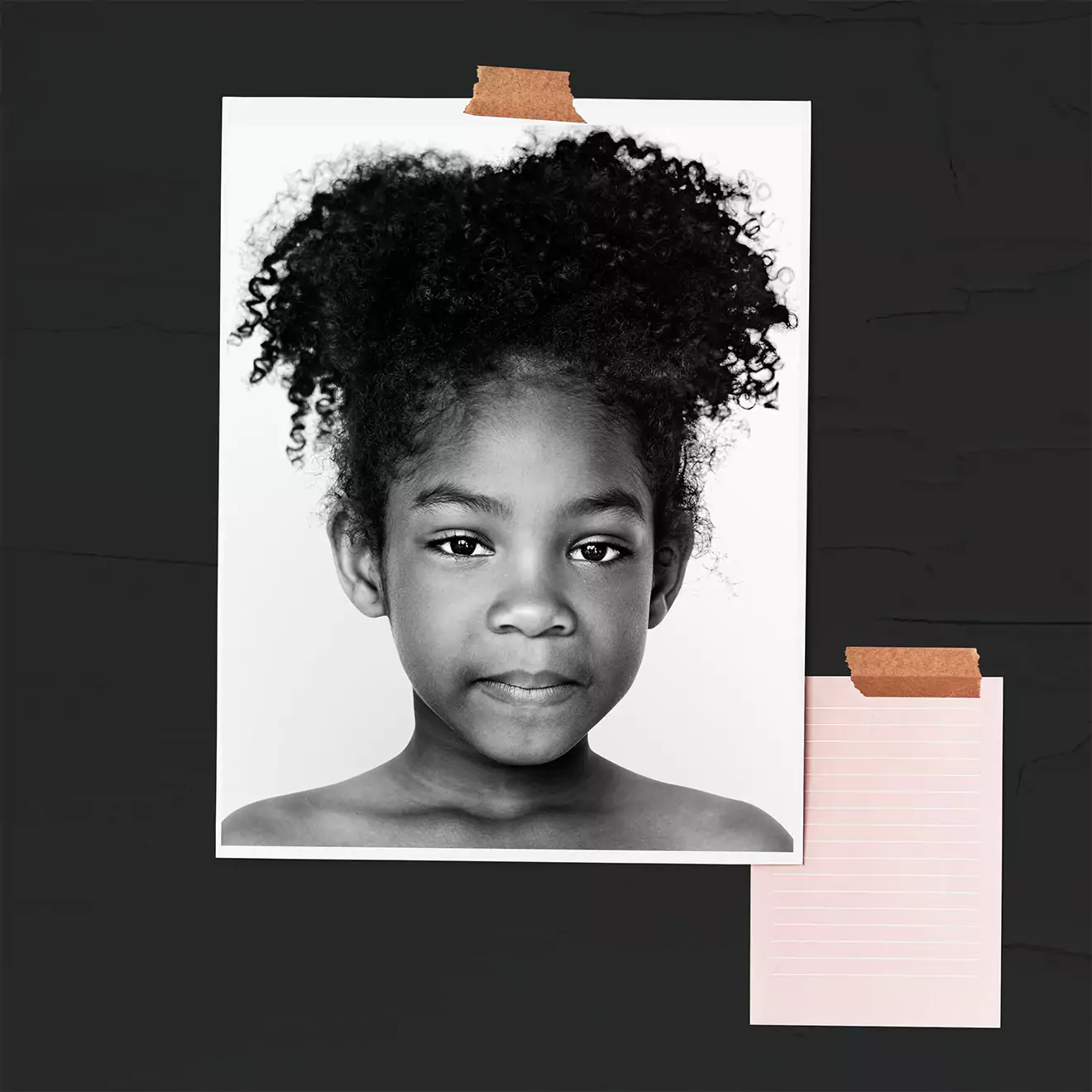 Black and white wall art featuring a close-up portrait of a young child with curly hair, taped to a dark background. A smaller blank piece of paper is taped below the portrait.