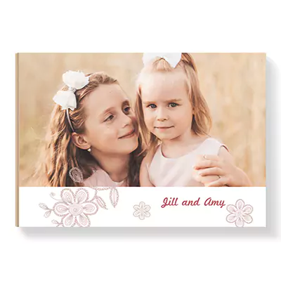 Pretty Pink theme hardcover photobook featuring a soft pastel design with floral accents. The cover showcases a heartwarming photo of two young girls, with personalised text 'Jill and Amy' in elegant script. Ideal for gifts such as baby showers, Christmas, or Valentine's Day.