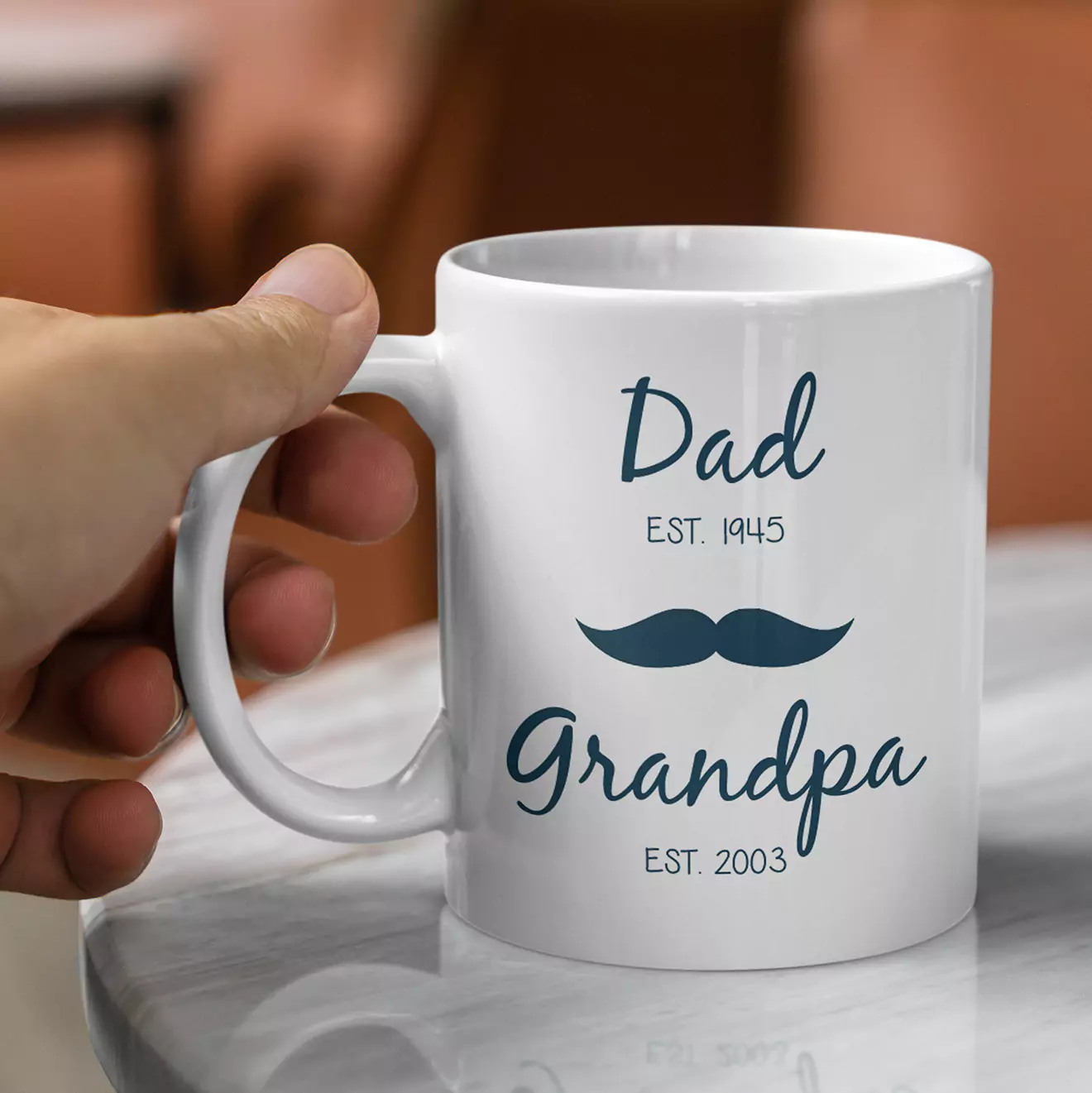 White ceramic mug with a handle, featuring a design that reads "Dad EST. 1945" and "Grandpa EST. 2003" in elegant blue script. The mug also includes a blue moustache graphic between the two texts. Ideal for gifts for dad or grandpa, suitable for various occasions like birthdays or Father's Day.