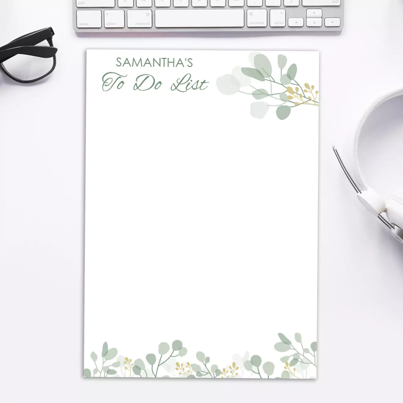 Personalised notepad with "Samantha's To Do List" printed at the top, featuring a minimalist botanical design with green leaves and small yellow flowers. The notepad is placed on a white desk alongside a keyboard, glasses, and headphones. Ideal for gifts for her or Christmas gift ideas.