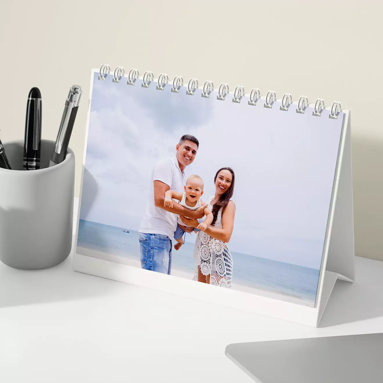 A personalised desk flipbook featuring a spiral-bound design with a photo of a smiling baby in a colourful inflatable ring. The calendar is propped up on a white triangular stand, with the phrase "Awesome days ahead!" printed below the photo. Ideal for gifts and keepsakes.