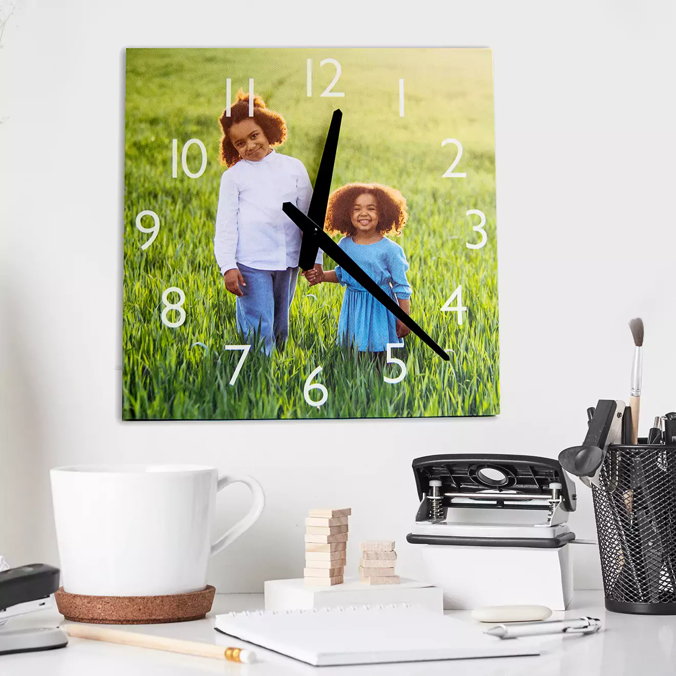 Square personalised wall clock featuring a custom photo of two children standing in a grassy field, with white numerals and black clock hands. Ideal as a unique gift for various occasions such as Christmas, birthdays, or Valentine's Day. Perfect for home or office decor.