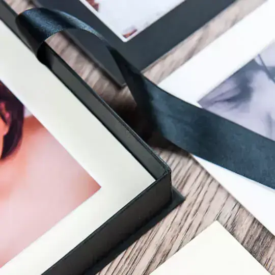 Close-up of a personalised photo album with a black ribbon bookmark, featuring high-quality printed photos on thick pages. The album has a sleek black cover and is displayed on a wooden surface. Ideal for gifts for men, baby shower gift ideas, and Christmas gifts.