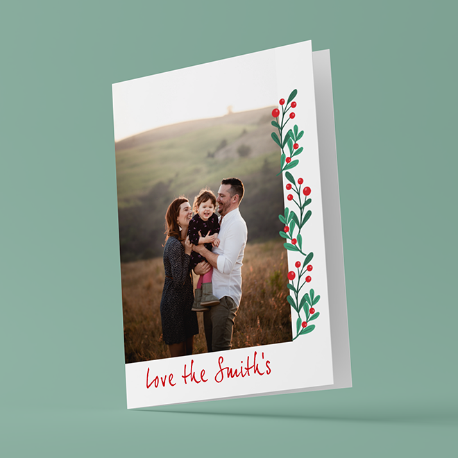 Personalised Christmas card featuring a family photo on the front, adorned with a festive design of green leaves and red berries along the right edge. The card has the text "Love the Smith's" in red at the bottom. Ideal for Christmas gifts and personalised holiday greetings.