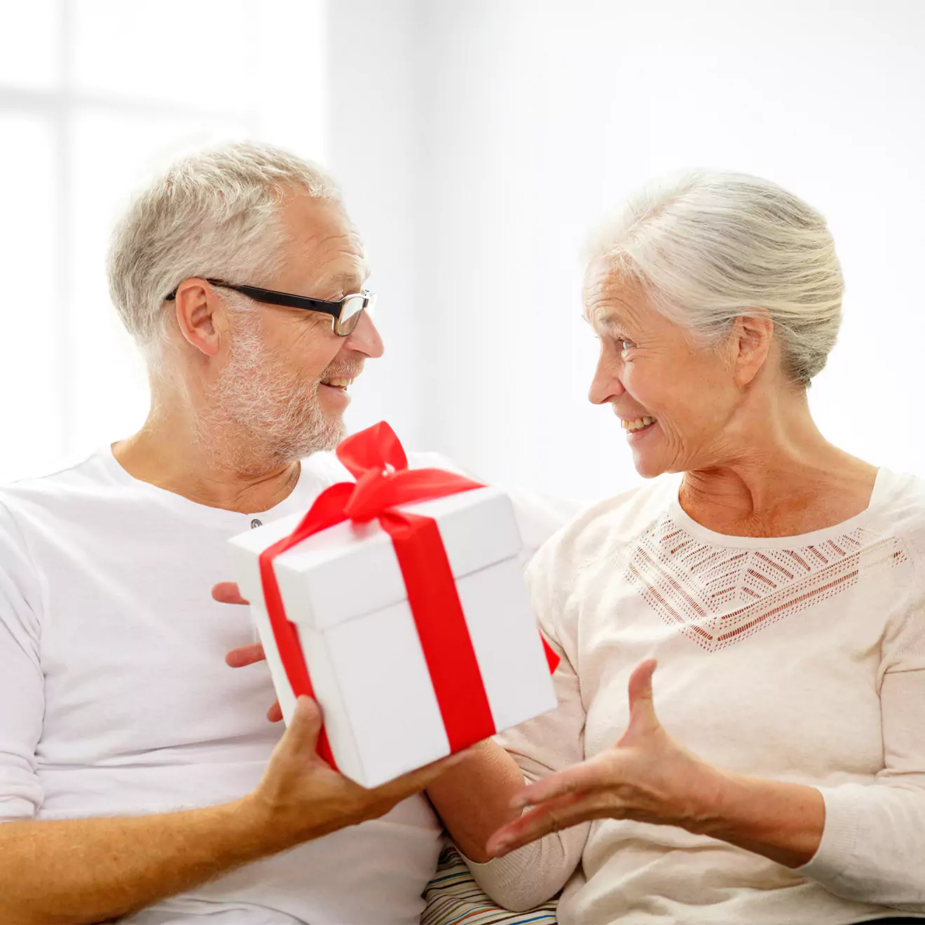 Image of an older couple exchanging gifts, looking at each other with affection, embodying timeless love and romance, perfect for inspiring those who are hopeless romantics at heart.