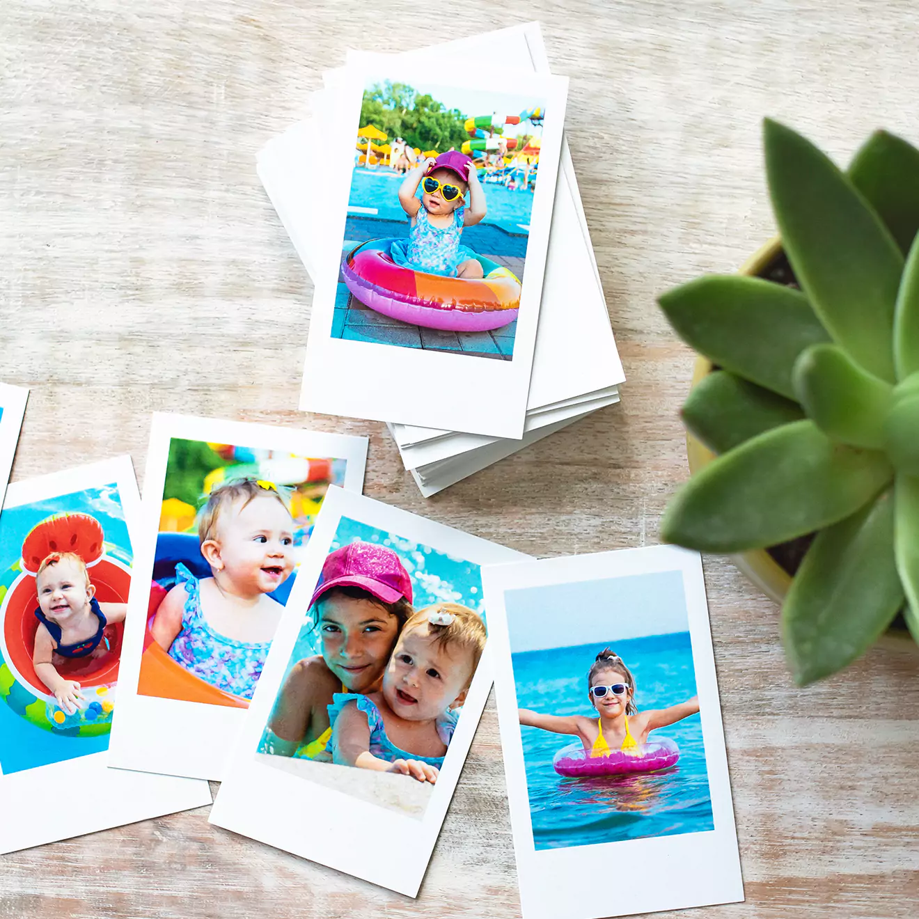 A collection of colourful, printed photo cards featuring various images of children and adults enjoying summer activities, such as swimming and playing in the pool. The photo cards are spread out on a light wooden surface, with a stack of additional cards in the background. Ideal for personalised gifts and photo albums.