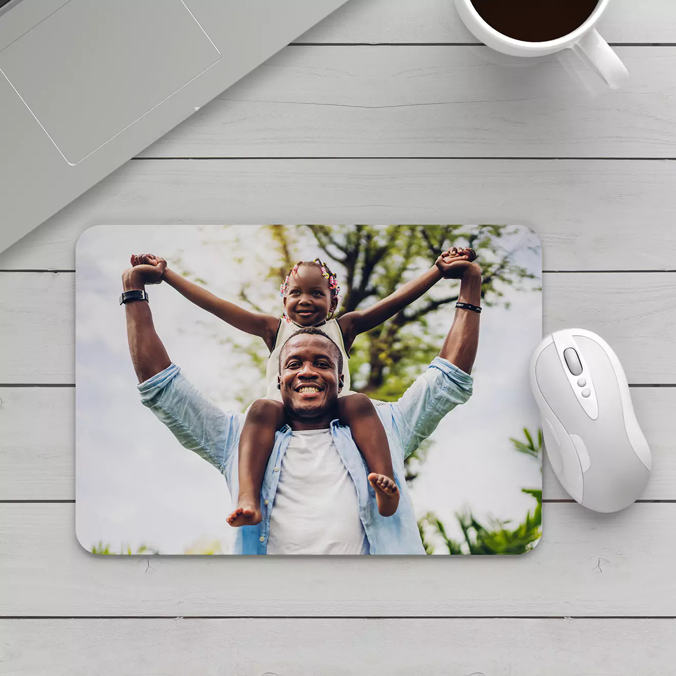 Customised mouse pad featuring a heartwarming photo of a father carrying his child on his shoulders, both smiling joyfully. The mouse pad is placed on a white wooden surface next to a white computer mouse. Ideal for personalised gifts, Christmas gift ideas, or gifts for dad.