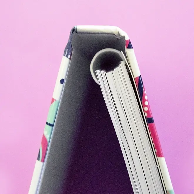 Close-up of a colourful hardcover photo book with a vibrant, abstract design on the cover, featuring a sturdy spine and high-quality pages. The book is propped open, showcasing its durability and craftsmanship, set against a pastel pink background. Ideal for personalised gifts in South Africa.