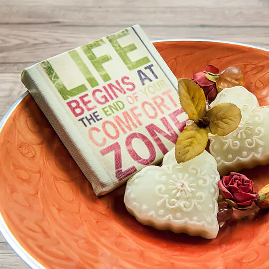 Decorative photo book with a motivational quote ''Life begins at the end of your comfort zone'' on the cover, placed in an orange bowl alongside heart-shaped white soaps and dried flowers. Ideal for personalised gifts in South Africa, photo albums, and unique gift ideas.