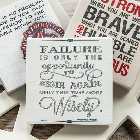 A square canvas with an inspirational quote in stylish black and grey typography, reading "Failure is only the opportunity to begin again, only this time more wisely." The canvas is placed on a wooden surface alongside other motivational canvases with different quotes. Ideal as a personalised gift.