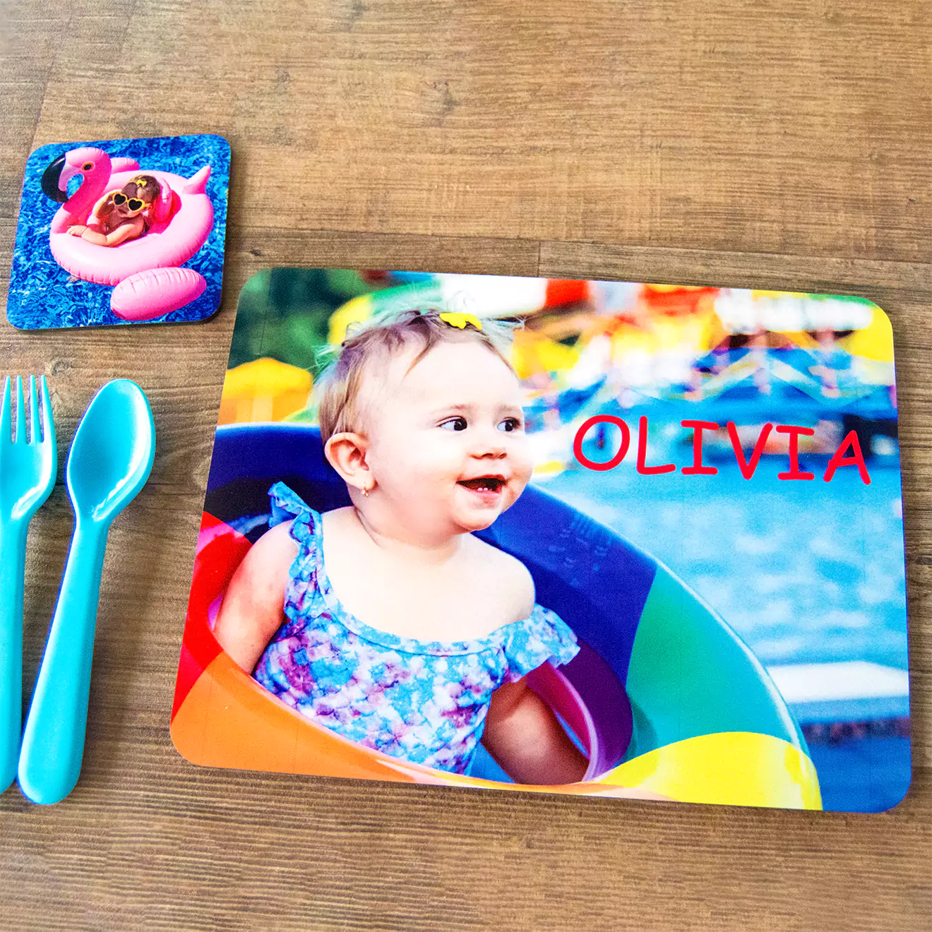 Personalised mouse pad featuring a colourful photo of a smiling baby girl in a blue dress with the name "Olivia" in red text. The background includes a vibrant, playful scene with a pool and inflatable ring. Ideal as a unique gift for various occasions such as baby showers or birthdays.