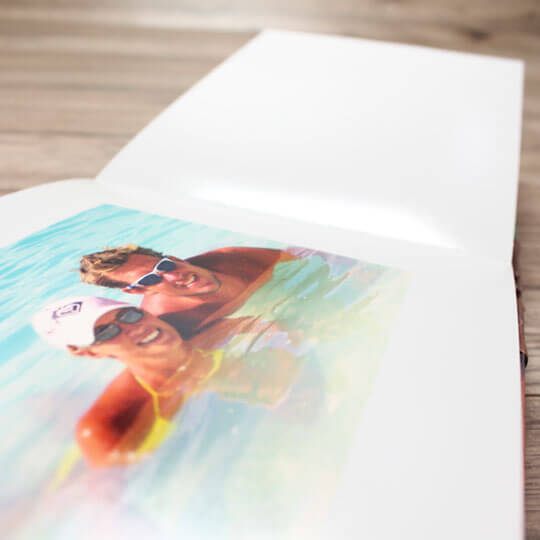 Open photobook displaying a high-quality image of two people in sunglasses enjoying a swim. The photobook lies on a wooden surface, showcasing its glossy pages. Ideal for personalised gifts in South Africa, photo albums, and special occasions.